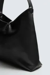 Bolso de hombro negro, de diseño liso y minimalista, con cierre metálico en el compartimento principal y un bolsillo interior con cremallera.