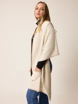 Poncho abierto de tejido de punto en color gris claro con bordes y detalles de bolsillos en gris oscuro. Presenta un diseño holgado y versátil con placa metálica decorativa en uno de los bolsillos frontales.