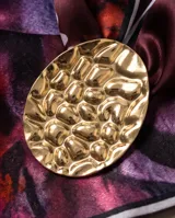 Pañuelo de seda con estampado multicolor en tonos violeta y burdeos, acompañado por un gran dije metálico dorado de textura martillada.