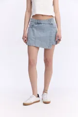 Short pollera de denim 100% algodón, de color celeste claro, con diseño cruzado en el frente tipo falda pareo y cierre lateral con botón.
