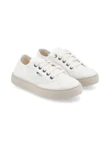 Zapatilla de lona blanca con suela de goma en tono beige. Presenta un diseño minimalista con cordones al tono y detalle de etiqueta pequeña en el lateral.