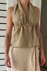 Top halter de lino color beige, con escote profundo en V y frunces ajustables en el torso. Presenta espalda abierta y tiras ajustables.