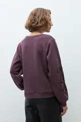 Sweatshirt color ciruela de cuello redondo y manga larga, con detalle de apliques bordados en relieve en las mangas.