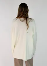 Sweater de punto gris con cuello redondo, mangas largas y diseño asimétrico, siendo más corto en la parte delantera y más largo en la trasera, con detalles de terminación en contraste.