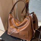 Cartera tipo hobo de cuero sintético color marrón, con diseño estructurado, bolsillo frontal con solapa y broche a presión, además de un compartimento diagonal con cierre metálico. Cuenta con asa para llevar al hombro.