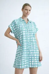 Vestido camisero de silueta relajada, con cuello clásico, cierre frontal de botones y mangas cortas con dobladillo. Presenta un estampado de cuadrícula irregular en color rojo sobre fondo blanco.