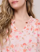 Blusa blanca de doble capa de gasa con estampado floral en tonos amarillos, celestes y rosados, escote en V con frunces y mangas cortas con volados amplios.