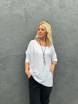 Blusa blanca de corte holgado y diseño minimalista, con cuello redondo y mangas largas. Presenta una textura sutilmente arrugada en la tela.
