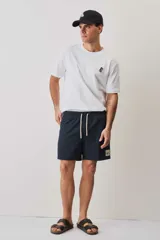 Short de baño de color azul marino, con cintura elástica y cordón ajustable blanco, bolsillos laterales y parche distintivo en el bajo. Presenta una textura con sutil efecto arrugado.