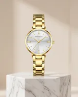 Reloj analógico para mujer con caja y malla de acero inoxidable en color dorado. Presenta una esfera minimalista con fondo blanco y marcadores de hora lineales.