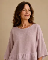 Blusa color rosado de corte holgado, con cuello redondo y mangas amplias de tres cuartos. Presenta un diseño con volados fruncidos en la parte inferior.