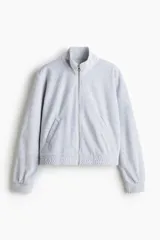 Campera corta de velour gris claro, de corte holgado, con cuello elevado, cierre frontal y bolsillos al bies. Presenta elástico fruncido en puños y bajo.
