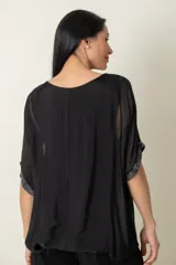 Blusa de seda negra con corte holgado, cuello redondo y mangas cortas tipo kimono. Presenta detalles de lentejuelas en los bordes de las mangas y en el ruedo inferior.