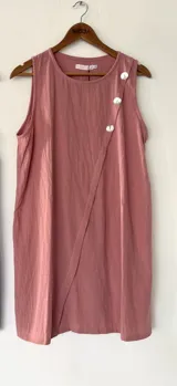 Vestido corto sin mangas de color rosado, con diseño cruzado en el frente y detalle de tres botones decorativos en la parte superior.