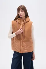 Chaleco negro sin mangas con capucha y cierre frontal. La parte superior es de tejido afelpado (tipo borrego o sherpa) y la parte inferior es de tejido acolchado liso.