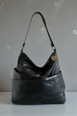 Cartera tipo hobo de cuero natural negro, amplia y de caída suave, con diseño envolvente, asa larga para el hombro y detalle de llavero metálico colgante.