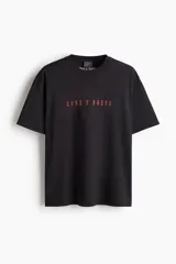 Remera negra de punto de algodón de corte holgado con hombros caídos, cuello redondo acanalado y estampa frontal con el nombre de la banda Guns N' Roses en color rojo.