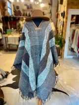 Poncho de lana virgen tejido en telar con diseño geométrico a rayas en tonos gris, marrón y celeste, con apliques de cuero en el escote y flecos en el ruedo.
