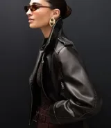 Campera estilo biker de cuero sintético color negro, con cuello solapa, cierre frontal asimétrico, bolsillos laterales con cremallera y detalles de botones metálicos en hombros y solapas.