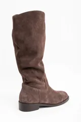 Bota de caña alta confeccionada en gamuza color marrón, con diseño de caña holgada y suela plana con pequeño taco cuadrado.