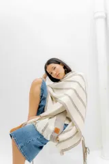 Ruana color crudo con rayas horizontales color marrón y flecos en el borde inferior.