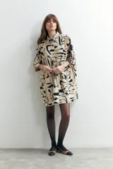 Vestido plisado color beige con estampado abstracto en negro, corte recto, cuello camisero y mangas cortas.