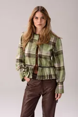 Blusa de tartán con diseño versátil, confeccionada en tela escocesa con detalles en cuero de oveja. Presenta cuello alto con forro de piel sintética, mangas largas con puños de cuero y piel, y un ruedo tableado con ajuste de cinturón de cuero en la cintura.