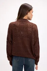 Cárdigan de tejido calado color blanco, con cierre frontal completo, cuello alto y mangas largas. Presenta un diseño con patrón de perforaciones geométricas y ajuste relajado.