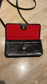Cartera tipo bandolera de cuero metalizado en tono azulado, con diseño rectangular, solapa con cierre magnético y detalle de trenzado central. Incluye correa regulable y placa metálica con logo.