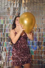 Vestido corto de fiesta color plateado con acabado brillante. Presenta un diseño de dos piezas que simula un conjunto de top y pollera, con aberturas laterales en la cintura, escote en V y tirantes finos que se cruzan en la espalda.