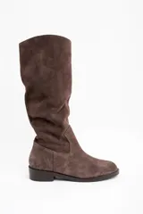 Bota de caña alta confeccionada en gamuza color marrón, con diseño de caña holgada y suela plana con pequeño taco cuadrado.