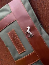 Sobre tipo cartuchera de lona con estampado de camuflaje y terminaciones en cuero marrón.