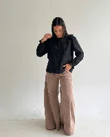Blusa negra de corte recto con escote redondo, mangas largas con puños elásticos y detalle de volados frontales con bordado central.