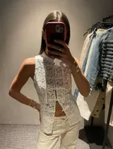 Top sin mangas de encaje blanco con cuello alto y cierre frontal con nudos de estilo asiático tradicional.