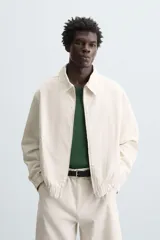 Cazadora de hombre color beige claro, de corte relajado, con cuello solapa, cierre frontal de cremallera y puños y bajo elásticos. Presenta una textura de rayas sutiles y efecto lavado.