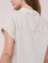 Camisa de lino de estructura recta, color beige con rayas verticales blancas. Cuenta con cuello solapa, escote en V abierto, abotonadura frontal, bolsillo plaqué en el pecho, mangas cortas de hombro caído y ruedo recto.
