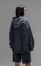 Hoodie oversize de algodón con diseño bicolor en gris oscuro y gris medio. Presenta capucha forrada, mangas raglán con recortes técnicos y un bolsillo frontal tipo canguro con un compartimento adicional con solapa.