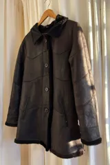 Campera tipo gamulán de cuero genuino en color marrón, con interior y detalles en corderito sintético color crema. Presenta cierre frontal con botones, cuello solapa y puños con vuelta.