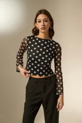 Top de manga larga confeccionado en tejido de tul semitransparente con estampado de lunares blancos sobre fondo negro. Presenta un corte ajustado al cuerpo, cuello a la base y mangas acampanadas.