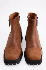 Botin de cuero vacuno color suela, con diseño de caña media, doble cierre lateral y suela track negra de goma.