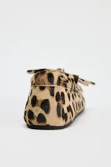Mocasín plano de piel con pelo con estampado animal print, detalle de flecos y lazo en la parte delantera, pespuntes en contraste y punta redonda.