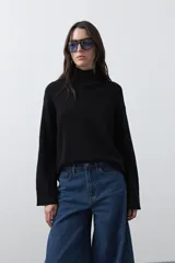 Polera de tejido liviano en color negro, con cuello alto, mangas largas y corte relajado. Presenta un diseño minimalista con recortes laterales que aportan estructura a la prenda.