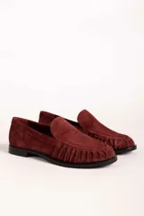 Mocasín de gamuza color bordó con detalle de frunces en la puntera y suela plana de goma negra.