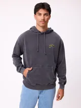 Canguro con capucha y cordones ajustables, de color gris claro. Presenta un logo bordado en el pecho y un parche decorativo en el puño de la manga derecha. Cuenta con un bolsillo frontal tipo canguro y puños acanalados.