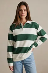 Sweater tipo polo de corte oversize con diseño de rayas horizontales anchas en color verde y blanco. Presenta cuello camisero con cierre de botones y mangas largas con puños ajustados.