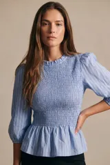 Blusa celeste a rayas con diseño de nido de abeja (smock) en el torso, cuello alto con volados y mangas largas abullonadas.