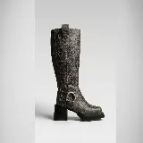 Bota de caña alta confeccionada en cuero vacuno con acabado texturizado efecto envejecido. Presenta punta cuadrada, plataforma delantera y taco cuadrado de madera. Incluye una tira decorativa con argolla metálica en la zona del tobillo y cierre lateral interno.