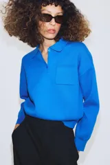 Jersey de punto con cuello tipo polo, manga larga con puños y cierre frontal con botones. Presenta un bolsillo de plastrón en el pecho y diseño de corte holgado.