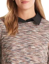 Buzo de tejido fino con efecto melange en tonos tierra, que incorpora cuello y ruedo inferior en tela tipo gasa negra, simulando una camisa debajo. Posee mangas largas y un diseño de corte recto.