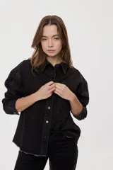 Sobrecamisa de denim negro con calce relajado, mangas largas, cuello clásico, cierre frontal con botones y bolsillo aplicado. Cuenta con detalles de strass en toda la prenda y terminación desflecada en el bajo.